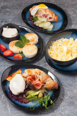 cheesecakes, porridge, croissants with salmon and ham on a gray background. Concept: Breakfast