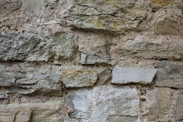 An old, ancient wall of weathered stones and bricks in a gray tone.