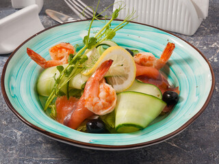 salad with shrimp, salmon, cucumber and olives, decorated with micro greenery and lemon