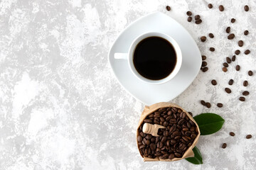 White cup of black freshly brewed coffee and a bag with grains nearby. Fresh, aromatic espresso. Gray background. Copy space