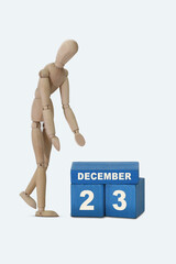 day of the month 23 December calendar . A calendar date on blue cubes and a wooden man standing next to it. White background