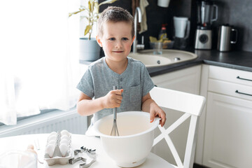 Cute caucasian boy bakes Christmas cookies or gingerbread cookies at home in the kitchen. Real authentic moments of life. Christmas or holiday preparation concept