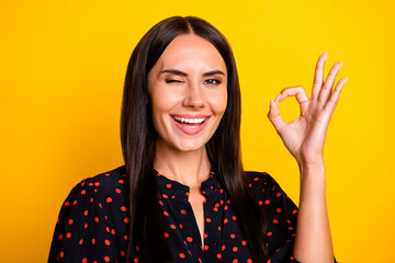Photo of funny flirty young lady dressed black clothes winking showing okey gesture isolated yellow...
