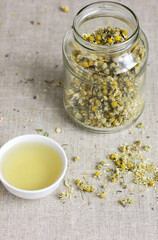 Chamomile herbal tea in chinese cup and glass jar with dry herb flowers, above overhead view, naturopathy, natural medicine, healing drinks for sleep, skin and hair care concept