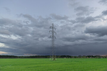 Elektryczny słup wysokiego napięcia na tle pokrytego ciemnymi, groźnymi chmurami nieba.