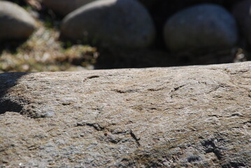 The uneven texture of a large granite stone. The textured surface of granite stone in different shades of gray, red and brown under the rays of the spring sun.