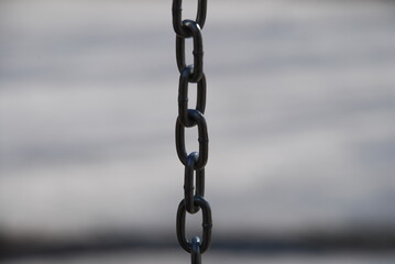 Metallic brushed chain on a white background. Part of the links of an iron gray chain with a classic anchor weave against a background of white snow. The rays of the sun are reflected from the links.
