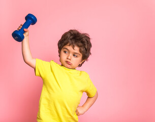 Little kid boy raises dumbbell. Funny strong child from kindergarten playing