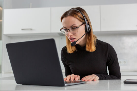 a girl in a black jacket and glasses stares at the computer screen in surprise, sitting at the kitchen table. Remote work. Home schooling. High quality photo