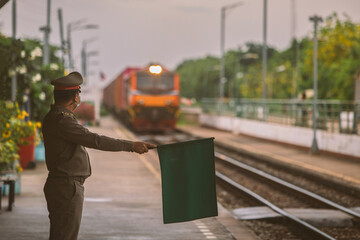 Master is waving green flag to make the train pass at platform of railway station in thailand