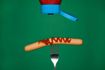 Sausage on a fork sprinkled with ketchup in a close-up view from the front on a green background