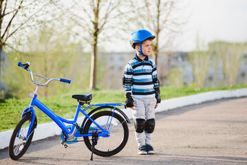 Cute child in helmet and protection stands near his bike