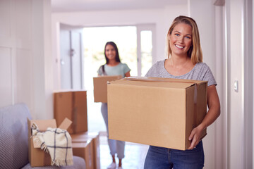 Fototapeta na wymiar Portrait Of Female Couple Carrying Boxes Through Front Door Of New Home On Moving Day