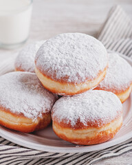 Delicious strawberry jam filled berliner doughnuts on white plate and glass of milk on wooden table...