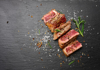 sliced fried beef steak New York  striploin on a black background with spices, degree of doneness rare