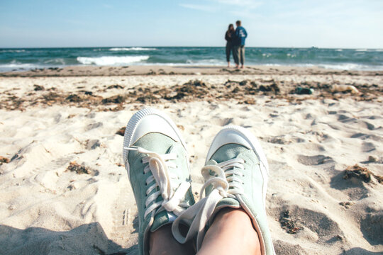 Girl in green sneakers resting on the beach. Summer beach and sea. Stormy sea, ocean © Rudaieva Iryna