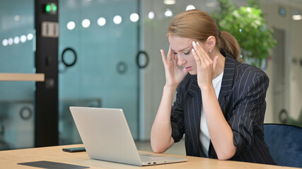 Stressed Young Businesswoman with Laptop having Headache in Office 
