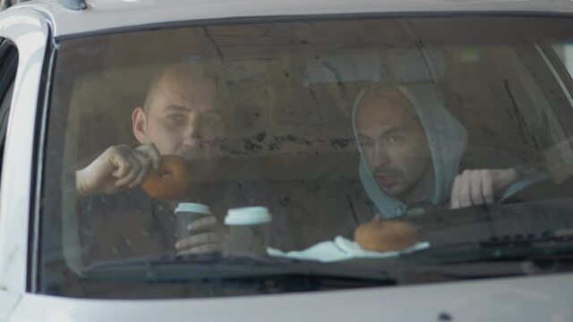 Two men sitting in a car and taking a picture with a professional camera, a private detective or a paparazzi spy.