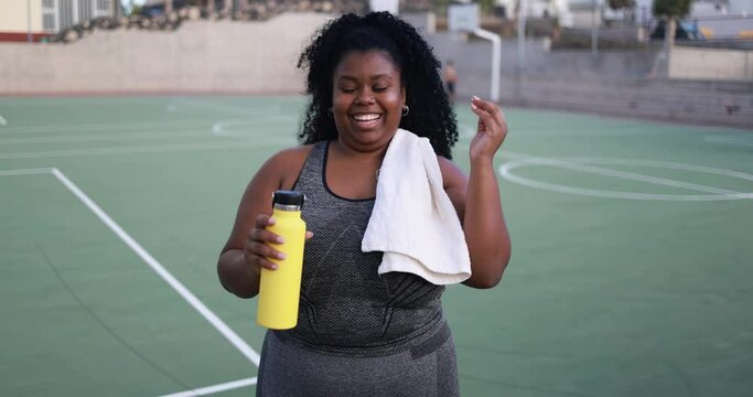 Curvy african woman smiling in camera while doing jogging routine outdoor in the city - Plus size and sport workout concept