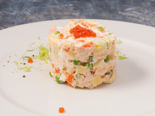 Olivier salad with salmon and red caviar on a white plate in a restaurant