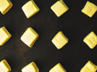 Square marshmallow on a dark background, yellow color, pattern, top view saturated yellow, textured background
