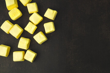 Yellow marshmallow, on a dark background, top view, scattered, square marshmallows, rich yellow, textured background