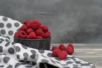 Red raspberries in bowl on grey wooden background