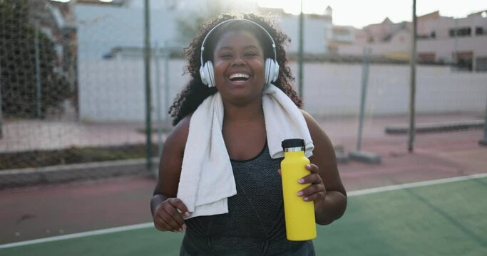 Curvy african woman smiling in camera while doing jogging routine outdoor in the city - Plus size and sport workout concept