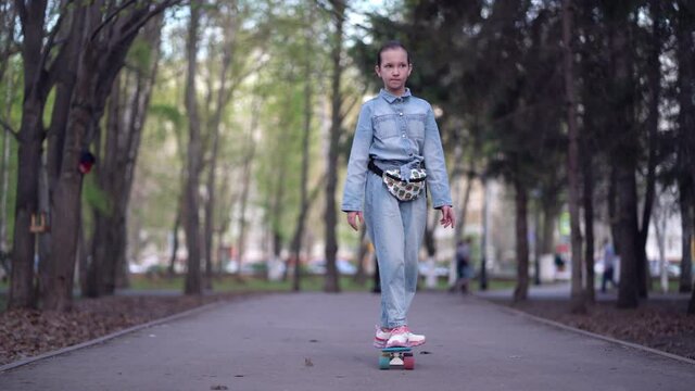 Fashionable girl travels through park streets on a skateboard