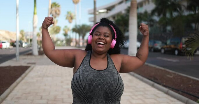Plus size african girl in the city posing showing biceps muscles - Curvy woman after sport workout outdoor - Sport and healthy lifestye concept