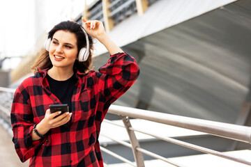 Young smiling woman outdoors. Beautiful woman listening to music while walking through the city