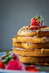 Stack of french toasts with fresh strawberries, raspberries, maple syrup, and powdered sugar on a plate. Tasty morning breakfast or brunch with gluten free bread. Easy making and healthy dessert. Side