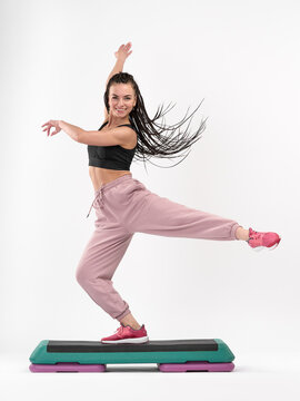 An attractive, smiling woman with Afro-pigtails is engaged in step aerobics. Isolated on a white background. Acrobatic element. Motion blur. Fitness Concept