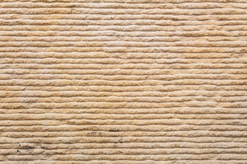 Yellow textured sand background, stone wall with horizontal wavy lines, in close-up