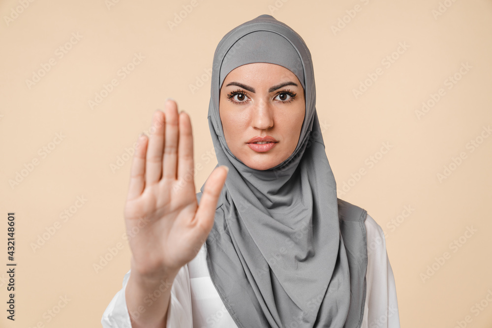 Wall mural nice-looking young serious islamic arabian middle eastern muslim woman in grey hijab showing stop wa