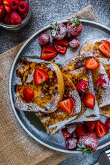 French toast with fresh strawberries, raspberries, maple syrup, and powdered sugar on a plate. Tasty morning breakfast or brunch with gluten free bread. Easy making and healthy dessert. Top view
