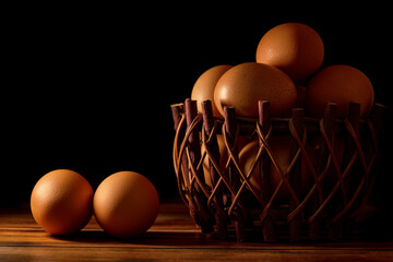 Chicken eggs in basket on wood against dark background.
