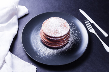 Chokolate pancake with white powder, on dark dish