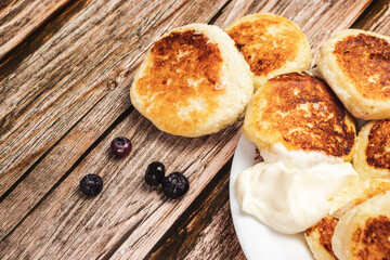 Cheese pancakes with sour cream in a close-up on a wooden background