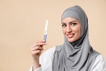 Happy young arabian muslim islamic woman wearing grey hijab holding pregnancy test isolated over white background. Positive pregnancy test, expecting a baby, future mom, fertility natality concept - obrazy, fototapety, plakaty