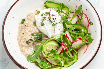 Breakfast oatmeal porridge with poached egg with vegetable salad of radish, cucumbers, arugula and microgreens. Food recipe background. Close up