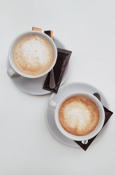 Overhead view of two cups of coffee on a table with sachets of sugar