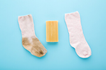 Baby socks and household soap on light blue table background. Pastel color. Closeup. Detergent for clothes washing. Compare between dirty and clean socks. Problem and solution. Top down view.