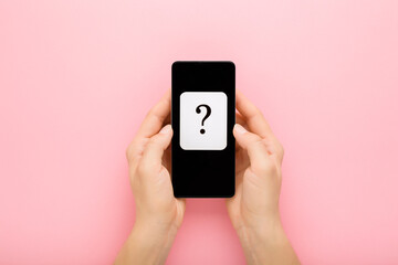 Young adult woman hands holding smartphone on pink table background. White card of question mark on...