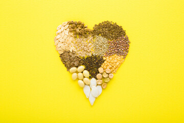 Heart shape created from dry different seeds on bright yellow table background. Closeup. Top down...