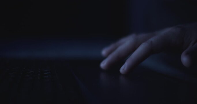 Close up of woman's hand using a laptop touchpad to browse the internet at night. Slow motion, shallow depth of field. 