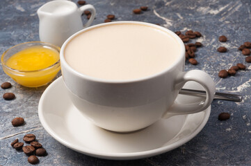 Cup of coffee with milk and honey on a gray background with coffee beans