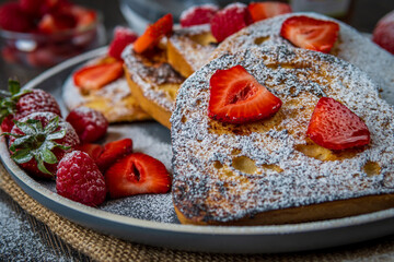 Closeup on french toast with fresh strawberries, raspberries, maple syrup, and powdered sugar on a plate. Tasty morning breakfast or brunch with gluten free bread. Easy making and healthy dessert.
