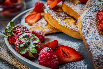 Closeup on french toast with fresh strawberries, raspberries, maple syrup, and powdered sugar on a plate. Tasty morning breakfast or brunch with gluten free bread. Easy making and healthy dessert.