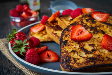 French toast on a plate with fresh strawberries, raspberries, maple syrup, and sugar powder aside. Tasty morning breakfast or brunch with gluten free bread. Easy making and healthy dessert. Side view